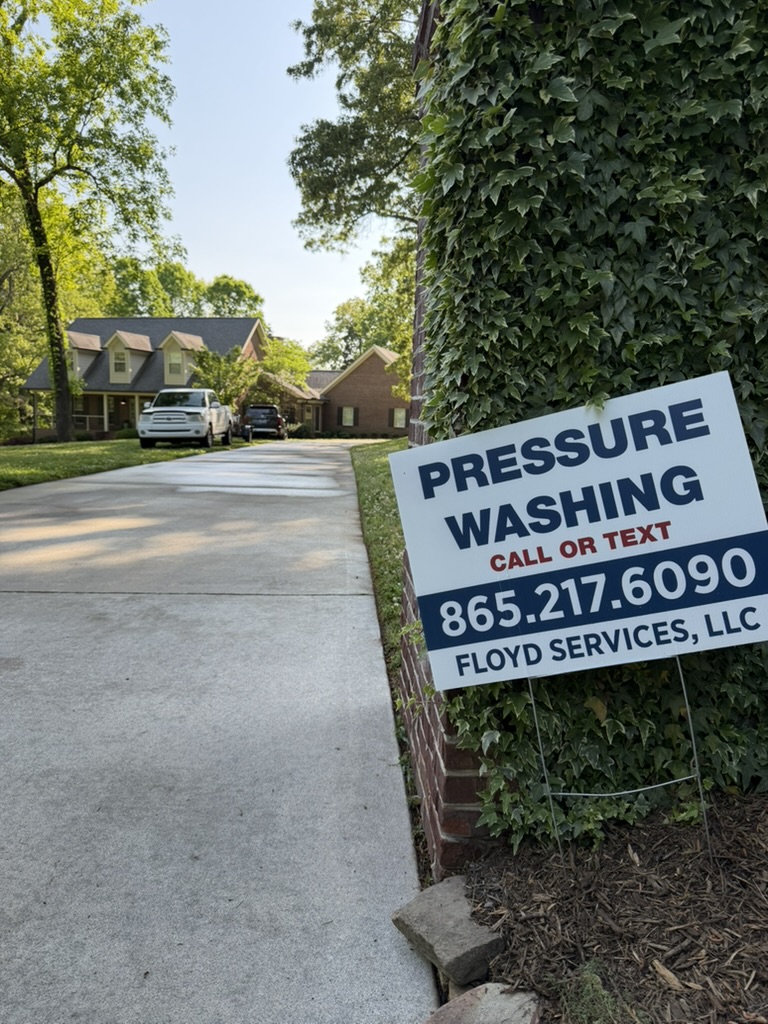 Clean concrete driveway and stone pathway after pressure washing with Floyd's Services sign